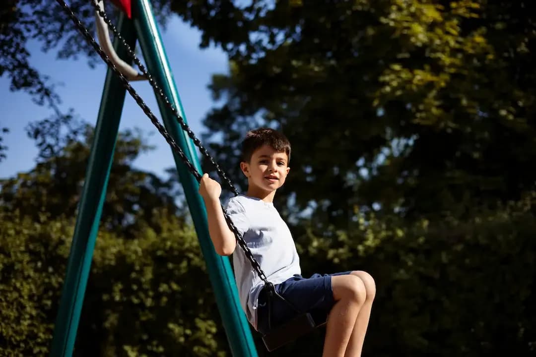 Menino brincando no balanço do parquinho infantil